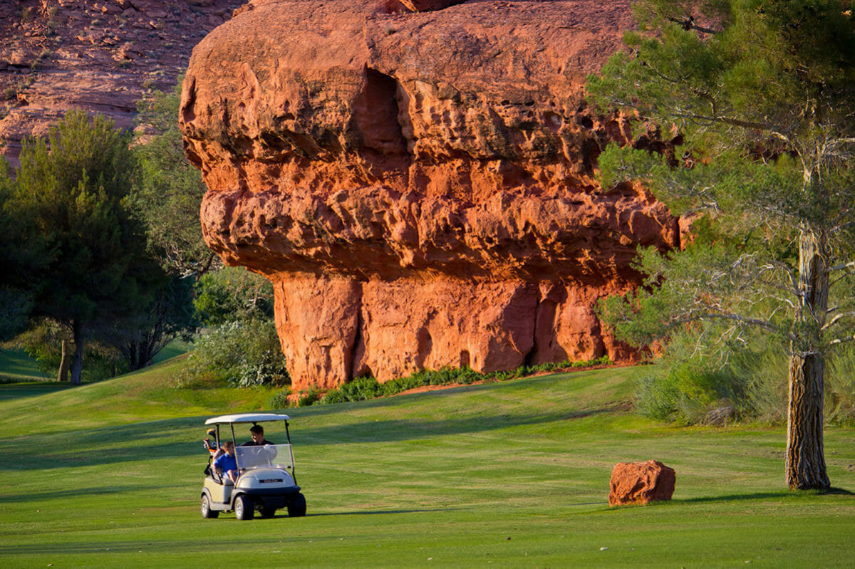 Father and son in golf cart on fairway in front large red rock formation.