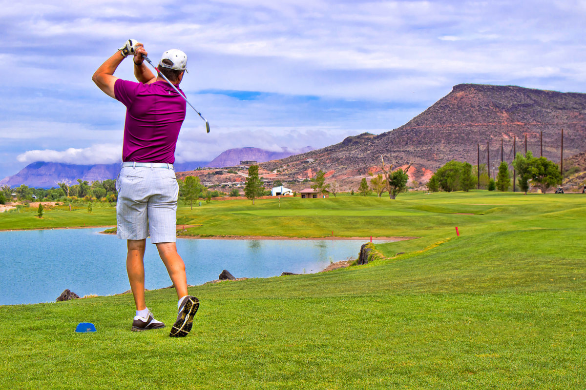 Male golfer in midswing in front of small pond.