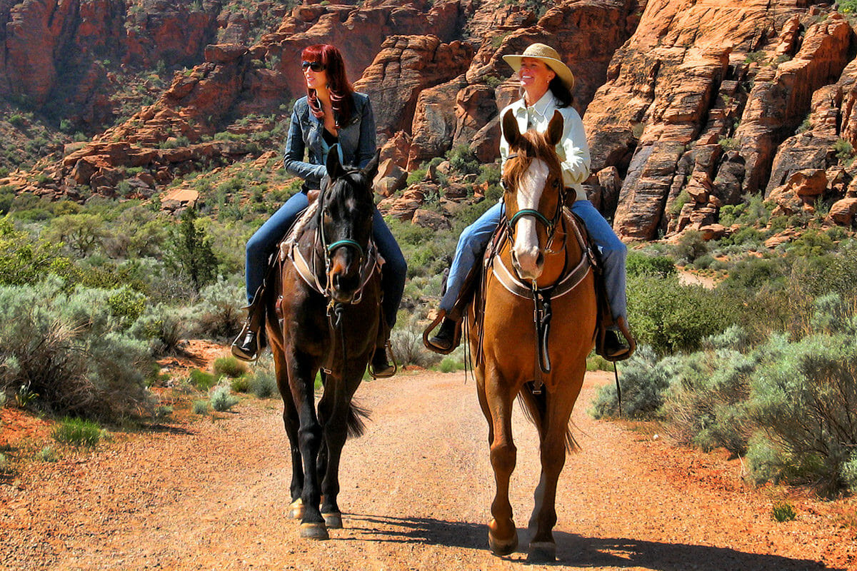 Two women riding horses through canyon.
