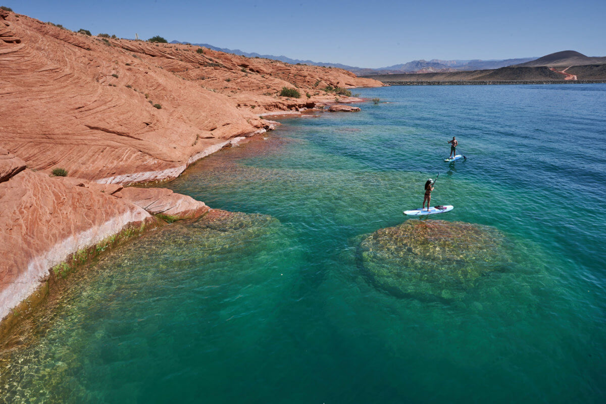 Couple paddleboarding on teal water with red rock formations