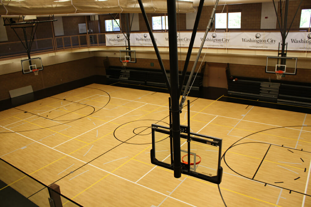 Basketball hoop suspended from ceiling above court with wood floor