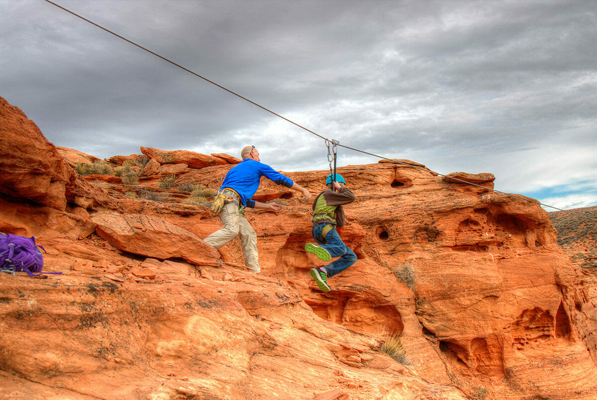Man pushing young boy off cliff on zipline.